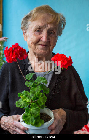 An elderly woman stands on the balcony with homemade flowers in hand. Stock Photo