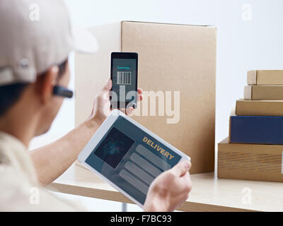 male asian courier company worker using cellphone and tablet computer to scan information on packages. Stock Photo