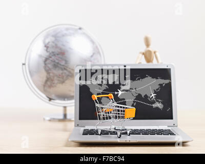 toy shopping cart on top of laptop computer with wooden dummy and world globe in background. Stock Photo