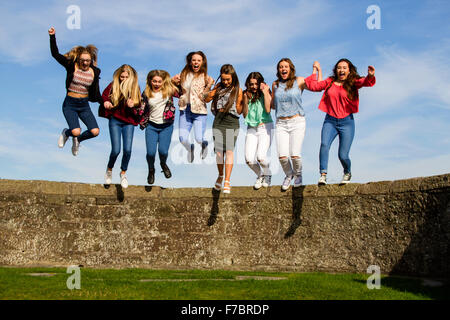 Eight teenage girls having fun holding hands and jumping off the Broughty Ferry Castle wall on a warm sunny day in Dundee, UK,