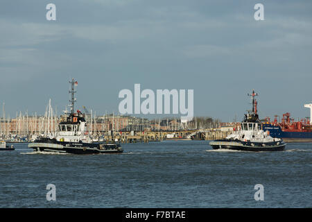 Matching tug boats heading out of Portsmouth harbour. White and black work boats preparing for the arrival of a container ship Stock Photo