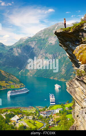 Tourist standing on the rock cliff, cruise ships in the background, Geiranger Fjord, Norway Stock Photo
