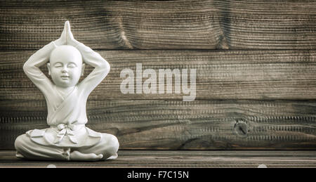 Sitting buddha. White monk statue on wooden background. Vintage style toned picture Stock Photo