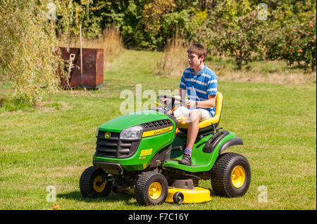 A 15 year old boy mowing the lawn on a John Deere ride on mower in the Uk Stock Photo