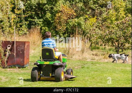 A 15 year old boy mowing the lawn on a John Deere ride on mower in the Uk Stock Photo