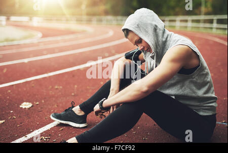 Young woman in sportswear sitting on stadium, listening to music and preparing for training Stock Photo