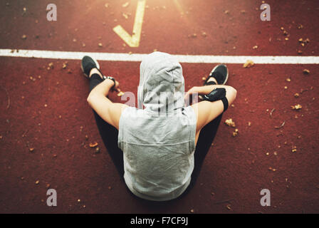 Back view of young woman in sportswear sitting on track field and preparing before training.Unrecognizable Stock Photo