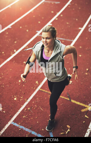 FIt young woman running on track field while listening to music Stock Photo