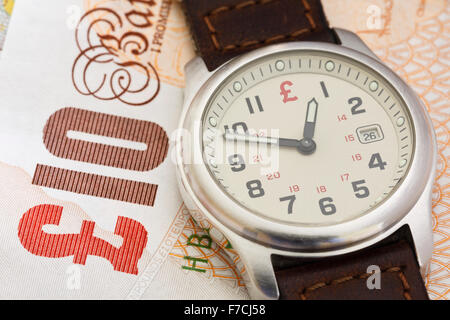 Wristwatch clock face on a British Sterling £10 ten pound note GBP to illustrate time is money concept. England UK Britain Stock Photo