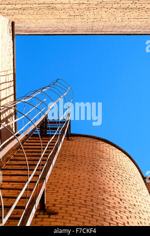 Industrial ladder, blue sky and brick walls of the building, bottom view. Stock Photo