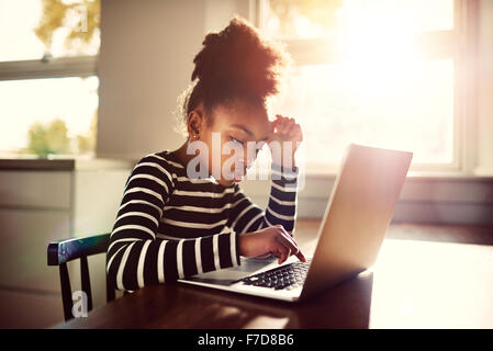 Young girl sitting at the dining table at home working on her homework from school typing out an answer on a laptop computer, e- Stock Photo