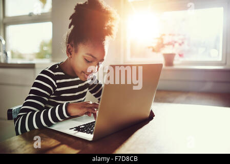 Ethnic girl with a cute afro hairstyle sitting at home using a laptop computer to do her class work and browse the internet, bri Stock Photo