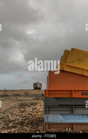 fishing crates stacked up with a disused boat on the beach midway under a backdrop of cloudy skies, Stock Photo