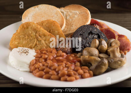 A traditional English Sunday breakfast consisting of beans, mushrooms, sausage, black pudding, english muffins egg and bacon. Stock Photo