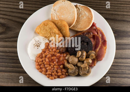 A traditional English Sunday breakfast consisting of beans, mushrooms, sausage, black pudding, english muffins egg and bacon. Stock Photo