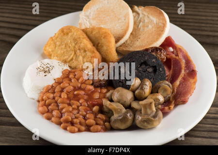 A traditional English Sunday breakfast consisting of beans, mushrooms, sausage, black pudding, english muffins egg and bacon. Stock Photo