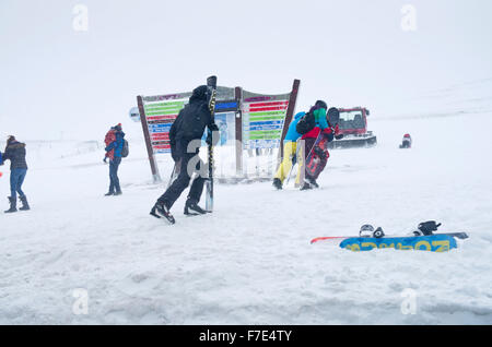 Skiers, snowboarders and tourists in a snowstorm outside the top station on Cairngorm Mountain, by the Piste information board. Stock Photo