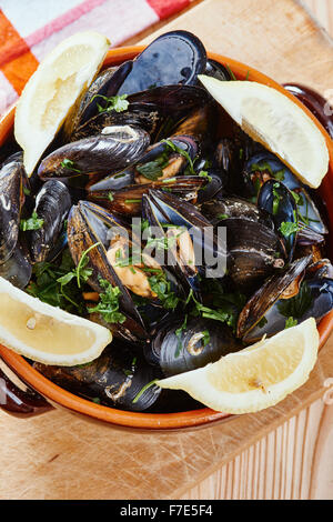 Mussels in a pot on the cutting board, lemons, tablecloth on wooden table