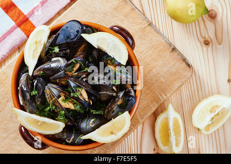 Mussels in a pot on the cutting board, lemons, tablecloth on wooden table Stock Photo
