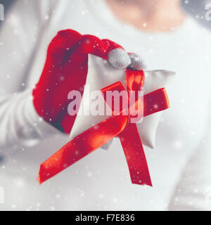 Woman giving Christmas gift wrapped with red ribbon decoration, holiday season with snowflakes falling, retro toned image with s Stock Photo
