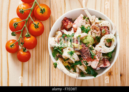 Seafood salad in white bowl, tomato, on light wooden table Stock Photo