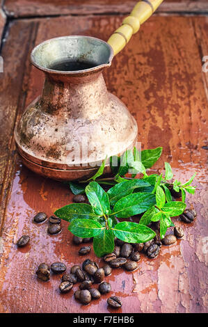 empty cezve on wooden background with scattered coffee beans and mint. Stock Photo
