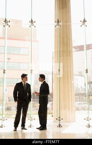 India, Two businessmen in suits talking in glass office lobby Stock ...