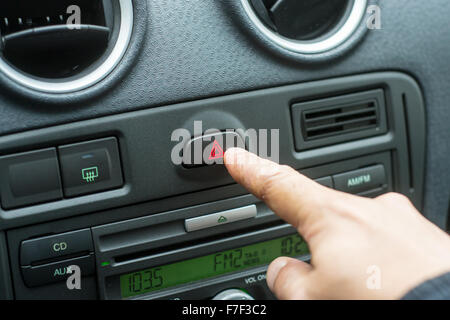 White male hand pressing the hazard button warning lights in a car Stock Photo