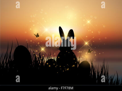 Silhouette of the Easter bunny sat in the grass against a sunset sky Stock Photo