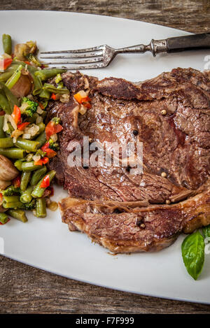 grilled beef steak with ground pepper and basil on wooden table