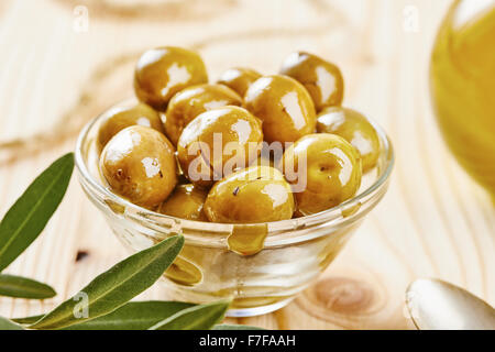 Olives in glass bowl, cruet, spoon and olive branch on wooden table Stock Photo