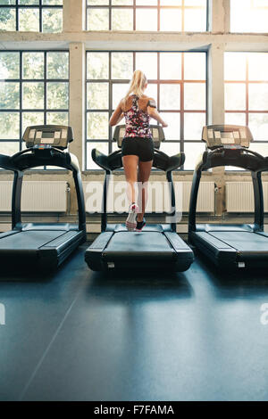 Rear view of young female running on treadmill in gym. Fitness woman jogging indoors in health club Stock Photo