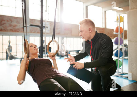 Male instructor helping a young female during a workout at gym on the rings. Personal trainer motivating young woman at health c Stock Photo