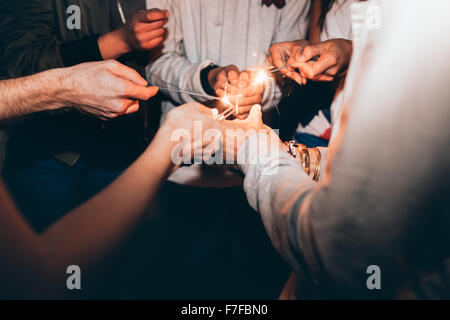 Close up shot of sparklers in hands of young people. Best friends celebrating new year's eve holding sparklers, in a party. Stock Photo