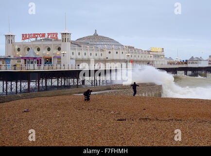 Brighton, UK. 30th Nov, 2015. With winds gusting to  60 mph and the pier in Brighton facing stormy seas,  one young man photographs another dancing in front of the breaking waves.  Scott Hortop/Alamy Live News Stock Photo