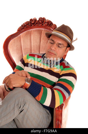 A middle age Hispanic man sitting in a pink armchair, with a bow tie and  cap, looking at his watch, isolated for white Stock Photo