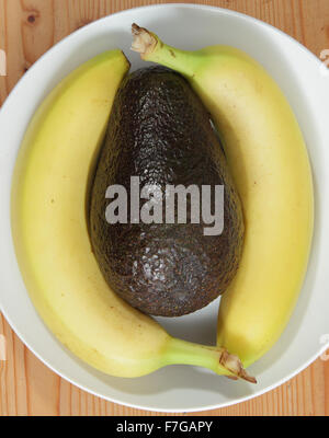 An avocado and bananas in a white porcelain bowl on a wooden background - domestic setting, england uk Stock Photo