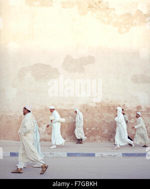 Moroccan Muslim men walk briskly past the city walls on their way to morning prayers. Essaouira, Morocco,North Africa. Stock Photo