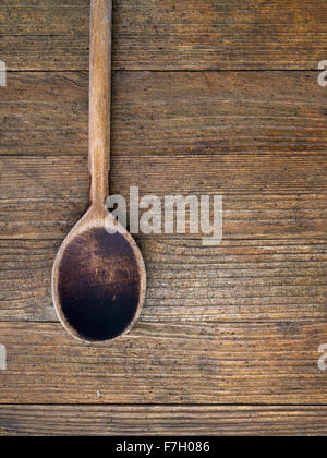 Old, well used wooden spoon on dark wooden background. Vertical composition. Stock Photo