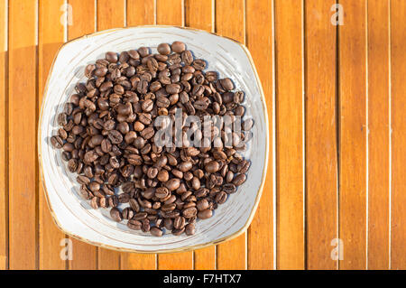 Coffee beans in a plate placed on a wooden table Stock Photo