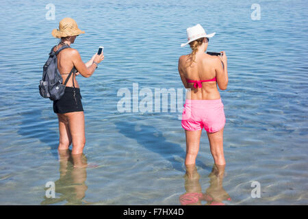 Two young female tourists taking selfies on beach Stock Photo