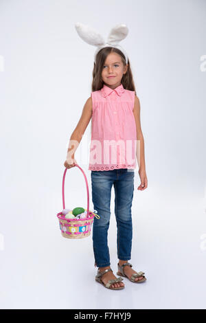 Full length portrait of a little girl with rabbit ears holding basket of eggs isolated on a white background Stock Photo