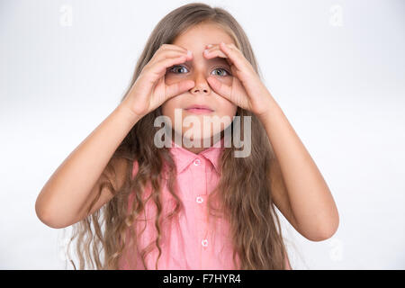 Portrait of a beautiful little girl looking at camera through fingers isolated on a white background Stock Photo