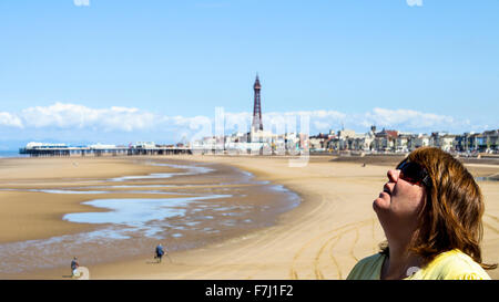 Blackpool, Lancashire, a mature woman looks up to the sky with the beach an tower in shot blue sky Stock Photo