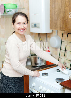 Happy mature housewife cleans the gas-stove  with sponge  in kitchen at home Stock Photo