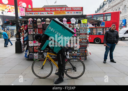 Black man with a Deliveroo takeaway courier bag on his back, standing astride his bike in Piccadilly Circus, London, England, UK Stock Photo