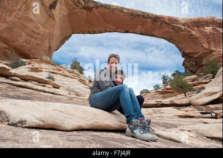 Mother and son sitting in front of Owachomo Bridge, Natural Bridges National Monument, Utah, USA Stock Photo