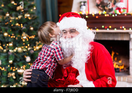 Santa Claus and little child boy. Kid telling his Christmas wish in Santa Claus near the Christmas opposite fireplace Stock Photo