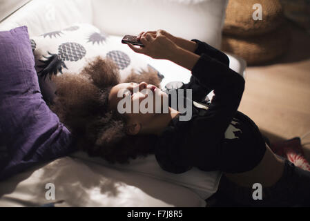 Girl reclining against sofa, engrossed in smartphone Stock Photo