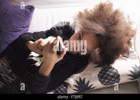 Girl lying on sofa using smartphone Stock Photo